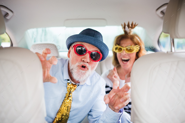 Cheerful senior couple with party accessories sitting in car, having fun - Stock Photo - Images