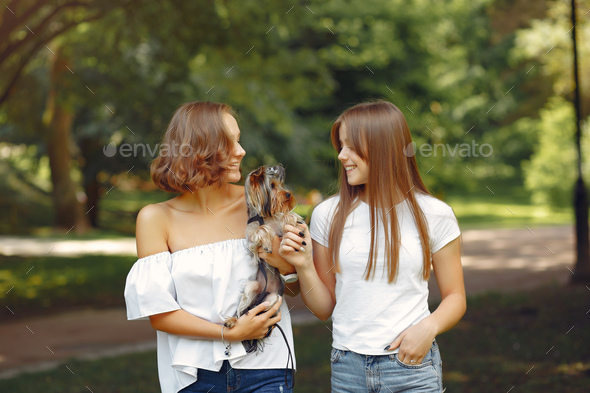 Two cute girls in a park playing with little dog