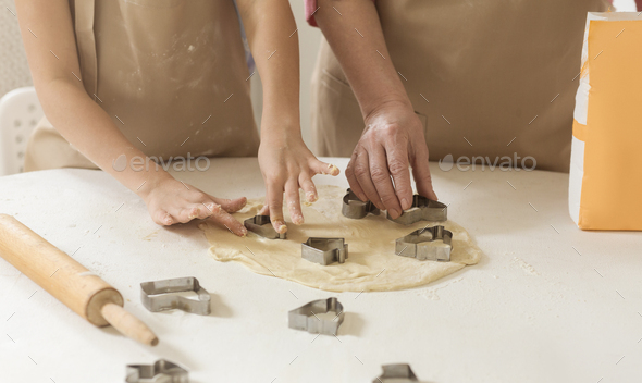 Home baking. Child and granny cutting cookies out of raw dough at table, closeup