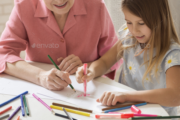 Mature woman with her lovely granddaughter drawing Christmas tree together in kitchen