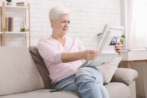 Senior lady squinting and holding newspaper far from eyes