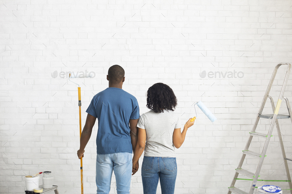 African american guy and girl with rollers in hands paint white brick wall