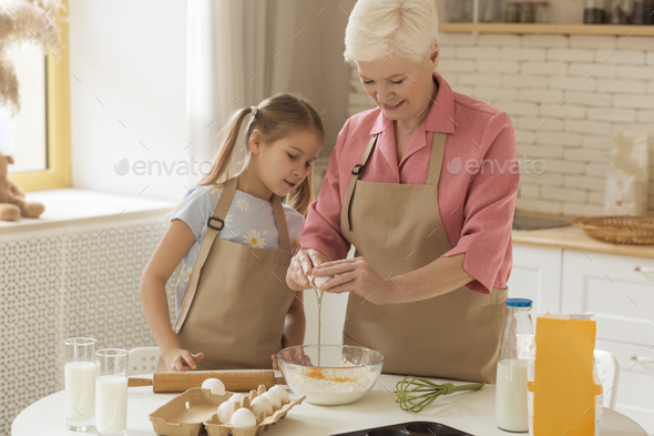 Baking together. Older lady and cute girl making dough together in kitchen