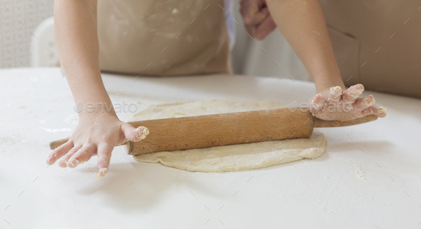Granny\'s baking class. Unrecognizable child rolling dough with grandmother at table, closeup
