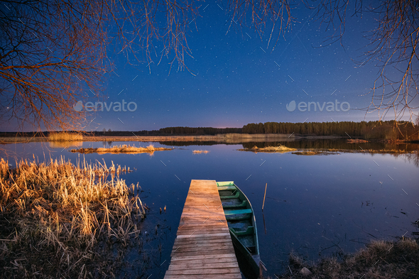 Belarus, Eastern Europe. Real Night Sky Stars Above Old Pier With Moored Wooden Fishing Boat - Stock Photo - Images