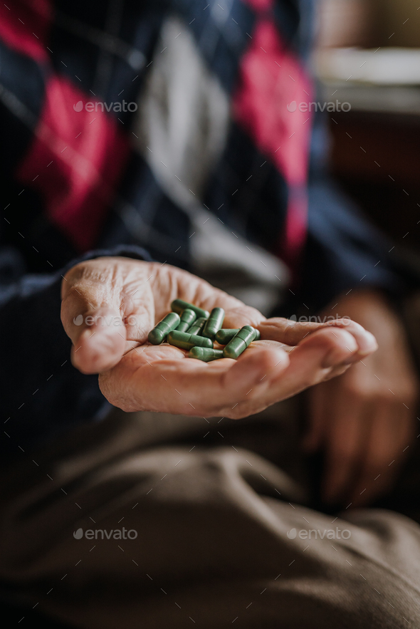 Old man holding handful of green pills in hand