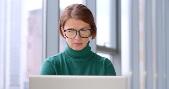 Portrait of a young woman in glasses working on a laptop.  alt