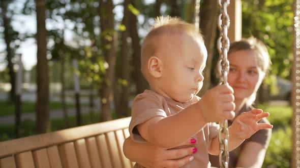 Mom and Son on a Wooden Rocking Bench on a Sunny Summer Day alt