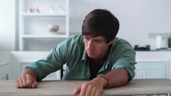 Portrait of Worried and Stressed Young Man Sitting at Table at Home alt
