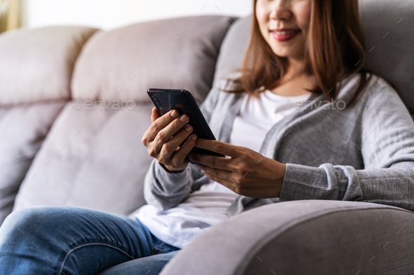 Young woman sitting on sofa at living room and using cell phone at home