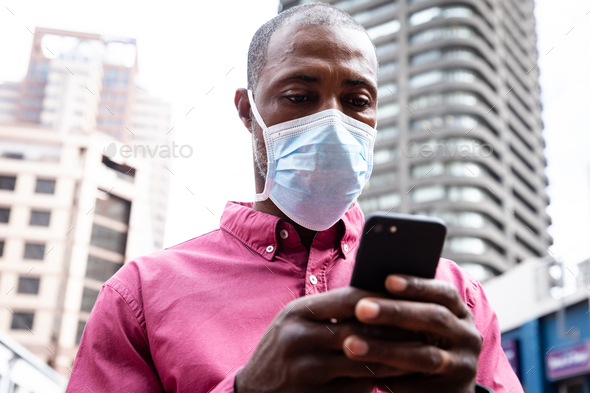 African American wearing covid19 coronavirus mask and using his smartphone in the street