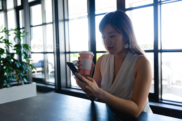 Asian woman using her phone and holding a mug