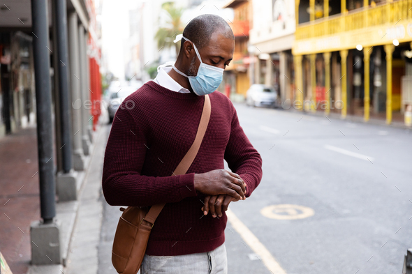 African American wearing covid19 coronavirus mask and using his smartwatch in the street