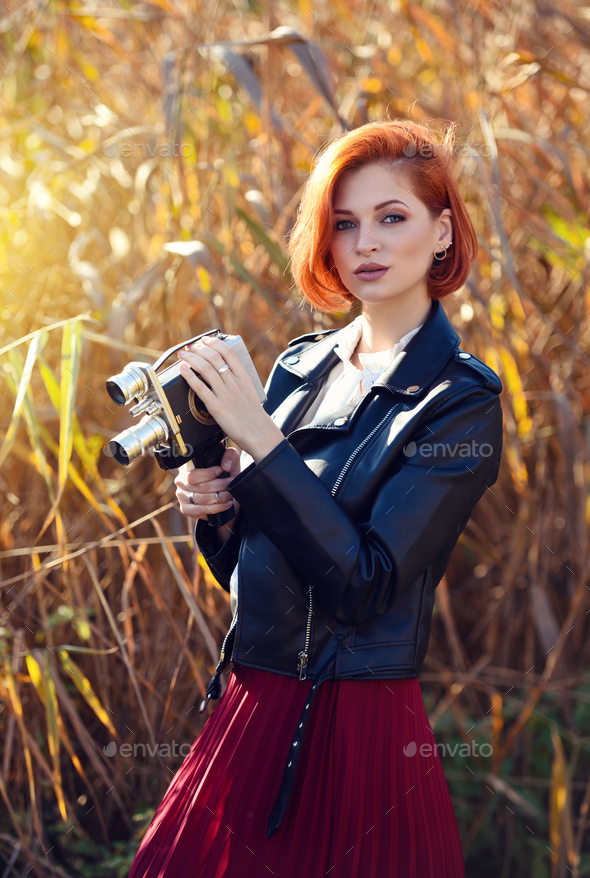 Beautiful young redhaired woman holds a video camera