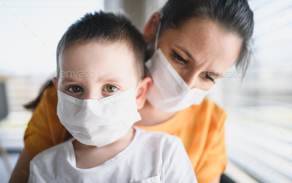 Mother and child with face masks indoors at home, Corona virus and quarantine concept