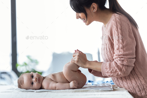 Smiling young mother has fun with little baby while changing his nappy at home. - Stock Photo - Images