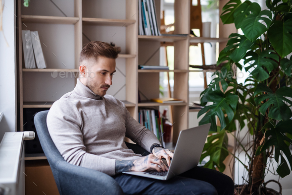 Young businessman sitting in armchair indoors in office, using laptop