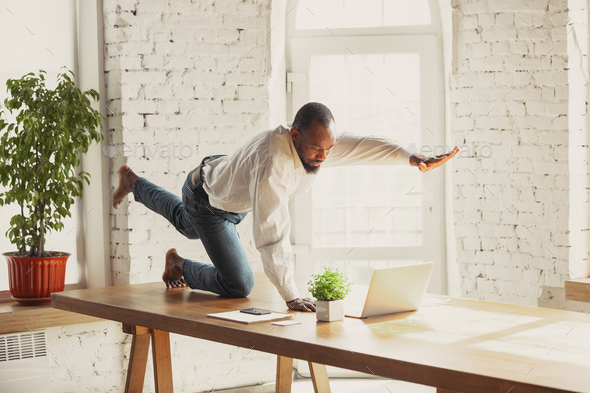 Young african-american man doing yoga at home while being quarantine and freelance working - Stock Photo - Images