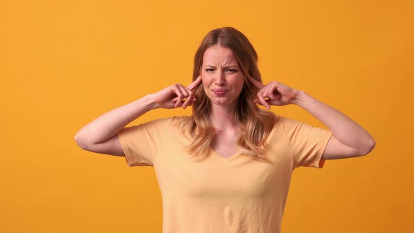 Sad blonde woman wearing yellow t-shirt plugging ears alt