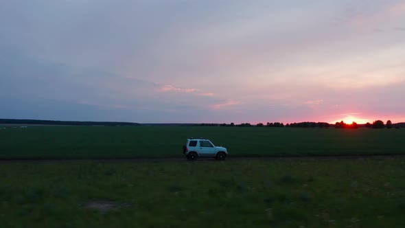 Aerial View of a Car Driving in Nature on a Field at Sunset alt