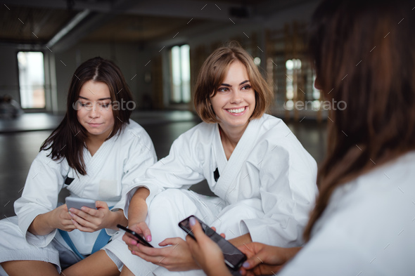 Group of young karate women with smartphones indoors in gym, resting.