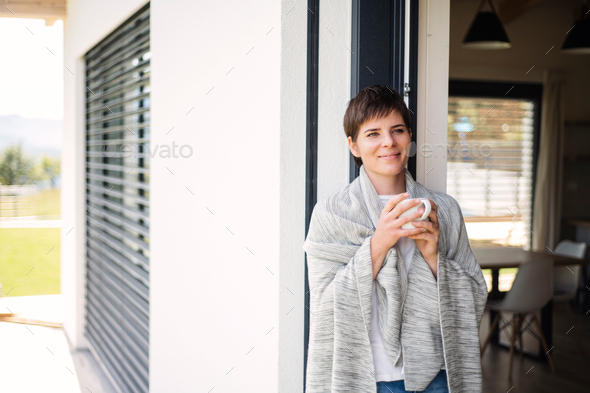 A young woman with coffee standing by patio door at home.