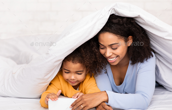 Mother And Daughter Using Cellphone Watching Cartoons In Bed Indoors
