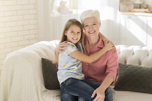 Friendship between generations. Cute kid with her granny hugging in sunlit room