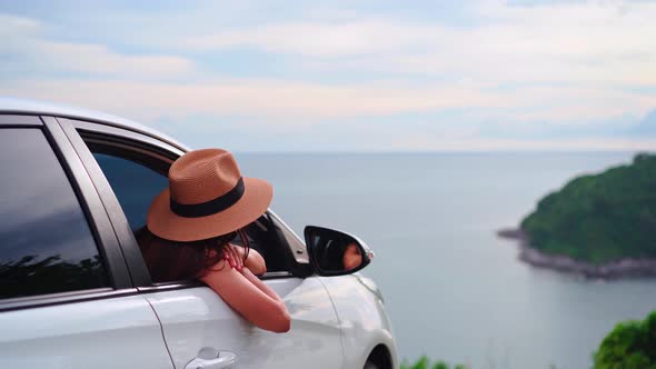 Young woman traveler looking at the beautiful sea view with her car while traveling