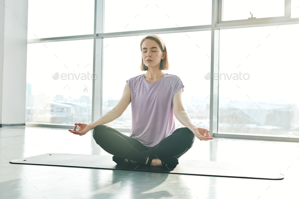 Serene woman in activewear sitting on mat while practicing lotus position