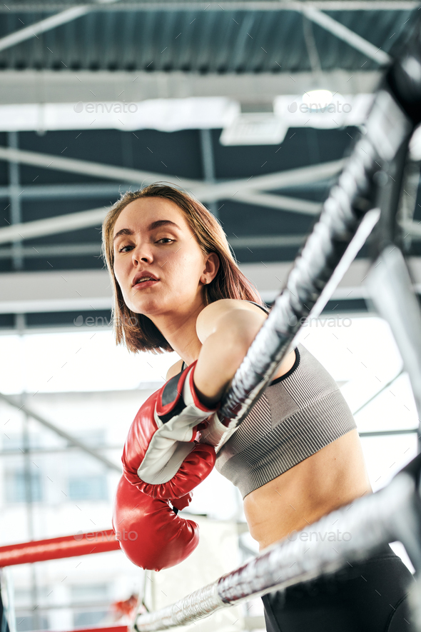 Pretty young confident female in activewear and boxing gloves standing by bars