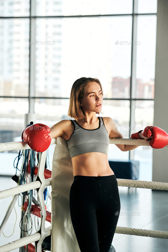 Young active female in red boxing gloves, grey crop top and black leggins