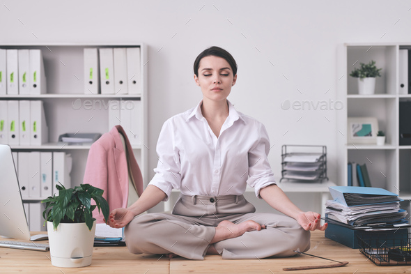 Pretty young barefoot businesswoman in formalwear sitting in pose of lotus