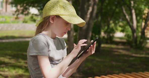 Little Girl Playing the Game on Her Smartphone While Sitting Outdoors alt