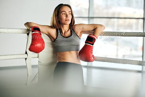 Young blonde woman in red boxing gloves and tracksuit having break