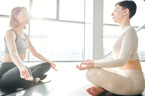 Two young relaxed females sitting in pose of lotus in front of each other