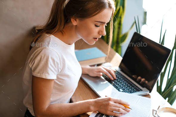 Photo of serious woman using laptop and studying with exercise book