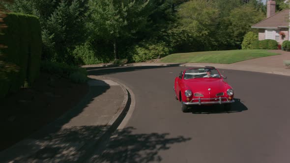 Tracking shot of man driving classic convertible car through neighborhood.  Fully released for comme