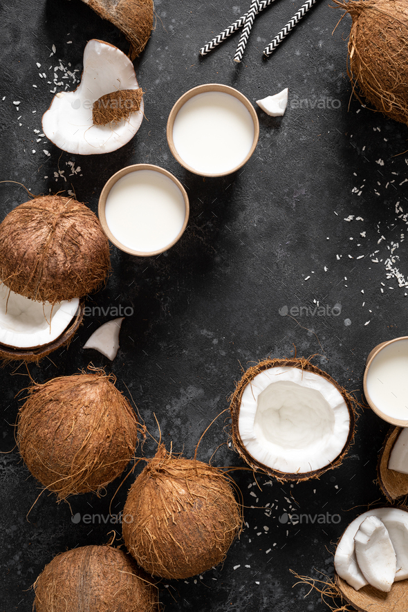 Coconut milk, whole and cracked coconuts on black background, top view