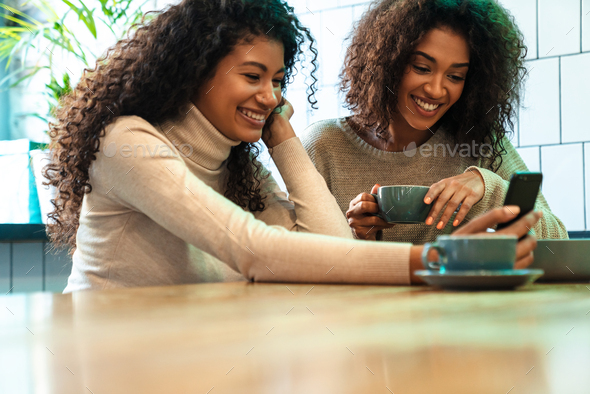 Two cheerful young african girlfriends sitting at the cafe