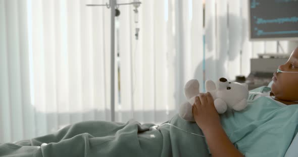 Side View of Cute African Girl Lying in Hospital Bed with White Teddy Bear alt