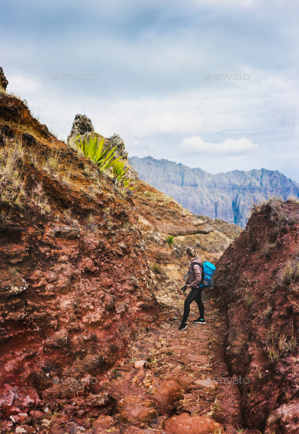 Female hiker with blue backpack staying on the stony cobbled trekking trail leading down to the Paul