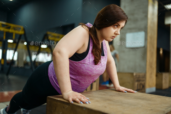 Overweight woman doing push ups exercise in gym