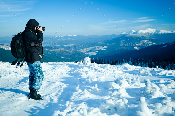Photographer standing with camera on hill with panoramic view of winter valley