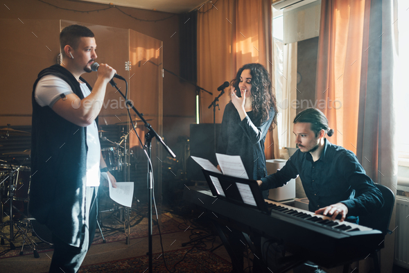 man sings microphone accompaniment electronic keyboards, teacher shows shape mouth vocal lesson - Stock Photo - Images