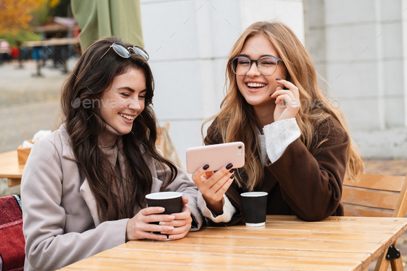 Two cheerful attractive women friends sitting at the cafe