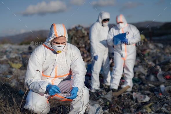 Group of activists with protective masks on landfill, environmental pollution concept