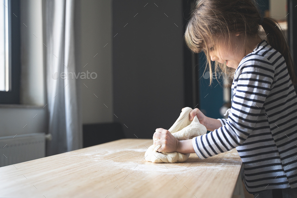little Caucasian girl working the dough on a wood cutting board - Stock Photo - Images