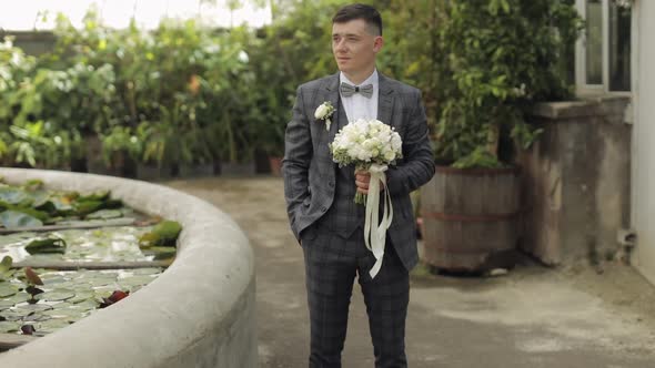 Groom Goes Down the Alley Between Bushes with a Wedding Bouquet To His Beloved Bride alt