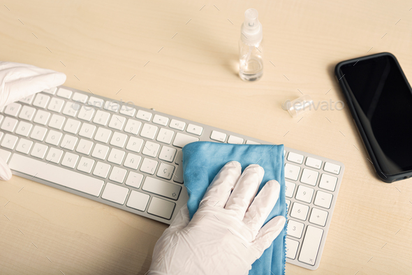 Hand with protective glove cleaning a keyboard with disinfectant